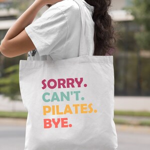 May include: White canvas tote bag with the text "SORRY. CAN'T. PILATES. BYE." in colorful letters.