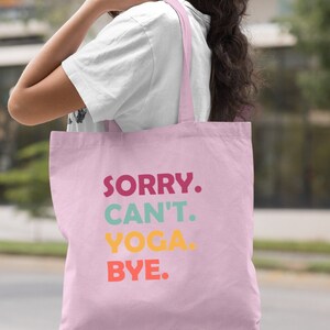 Puede incluir: Una bolsa de tela de color rosa claro con el texto "SORRY. CAN'T. YOGA. BYE." en letras de colores.