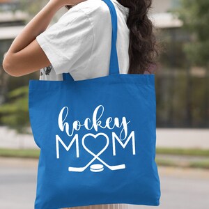 May include: A royal blue tote bag with white text that reads "hockey MOM" with a heart in place of the "O". The bag also features a white hockey stick and puck graphic.