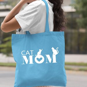 Peut inclure: Sac fourre-tout bleu clair avec du texte blanc qui dit "CAT MOM" et deux silhouettes de chats blanches.
