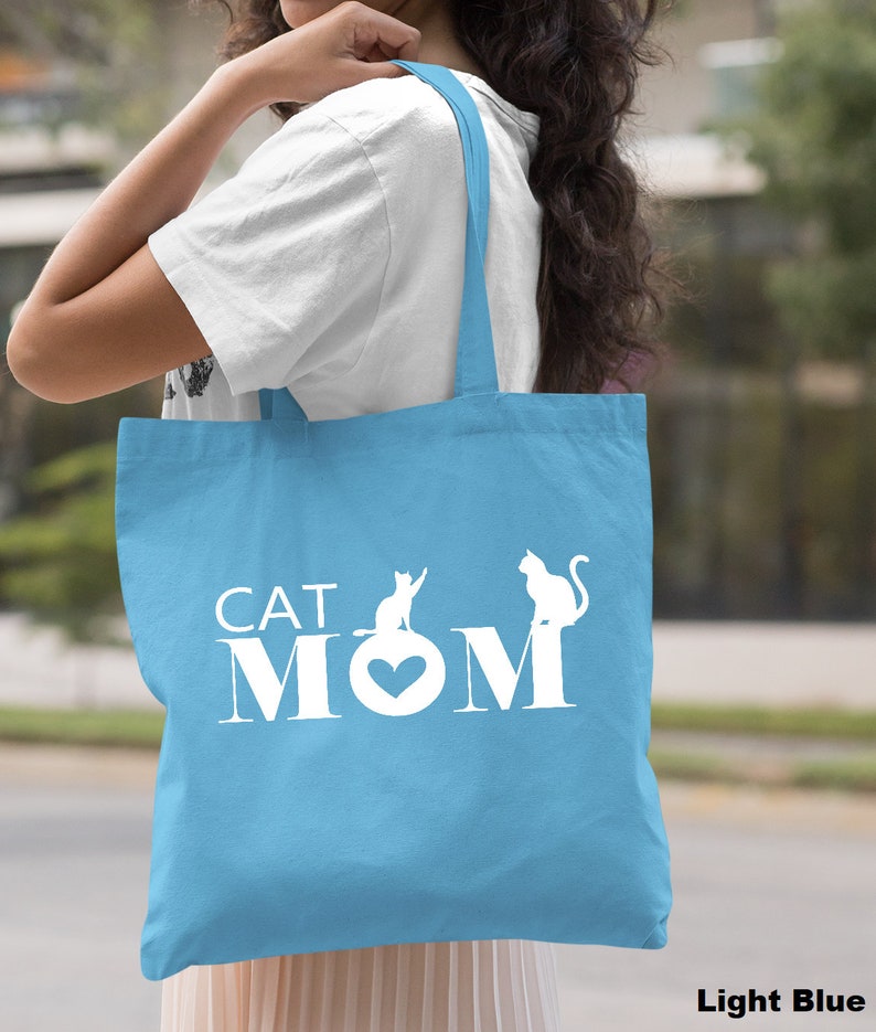 Peut inclure: Sac fourre-tout bleu clair avec du texte blanc qui dit "CAT MOM" et deux silhouettes de chats blanches.