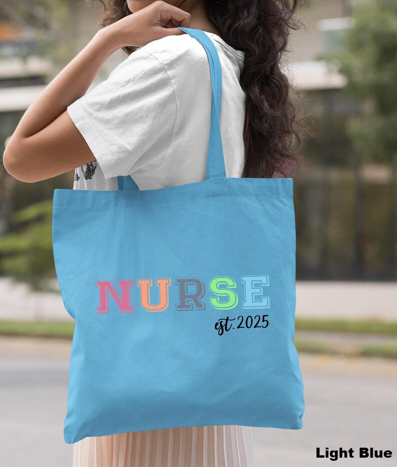 May include: Light blue tote bag with the word "NURSE" in rainbow colours and the text "est. 2025" in black.
