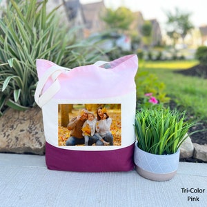 May include: A tri-color tote bag with a pink, white, and burgundy design. The bag features a photo of a family of three in a fall setting.