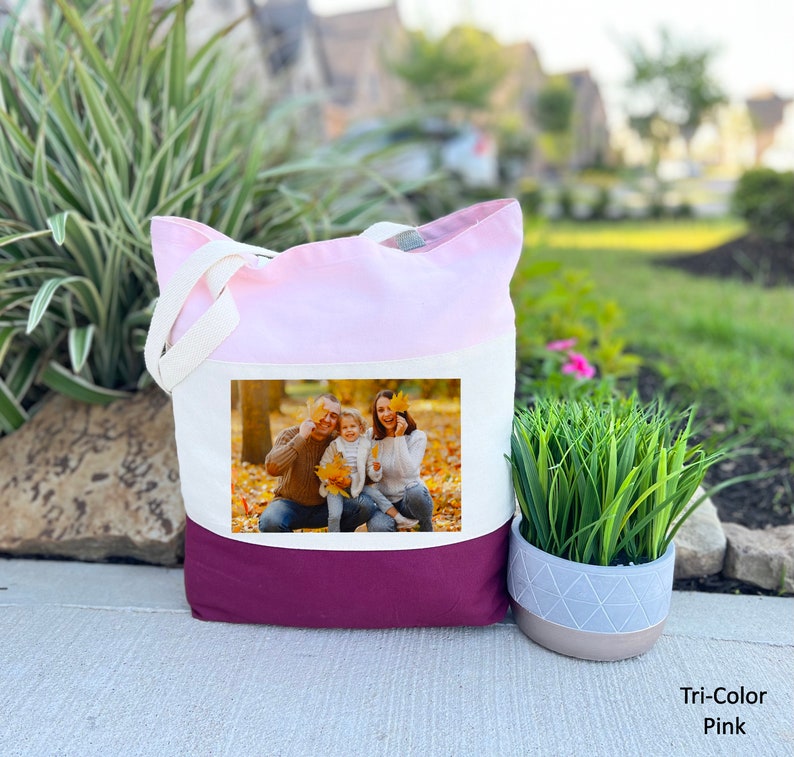 May include: A tri-color tote bag with a pink, white, and burgundy design. The bag features a photo of a family of three in a fall setting.