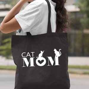 Peut inclure: Sac fourre-tout noir avec du texte blanc qui dit "CAT MOM" avec un c&oelig;ur dans le "O". Deux silhouettes de chats blancs sont de chaque c&ocirc;t&eacute; du texte.
