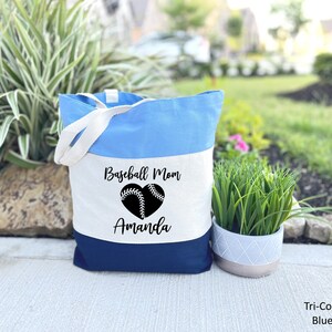 May include: A blue and white canvas tote bag with the text "Baseball Mom" and a baseball in a heart shape. The name "Amanda" is printed below the heart.