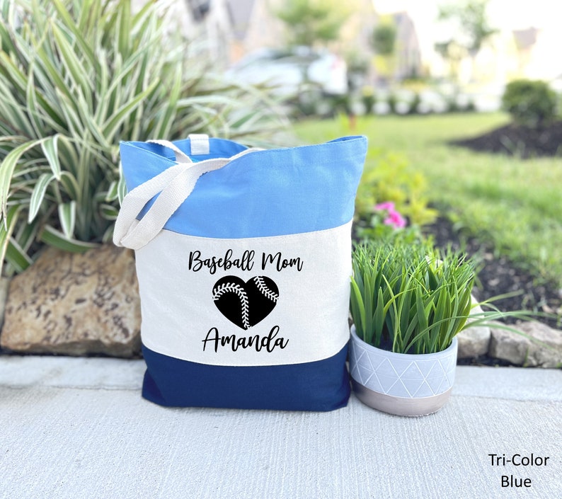 May include: A blue and white canvas tote bag with the text "Baseball Mom" and a baseball in a heart shape. The name "Amanda" is printed below the heart.