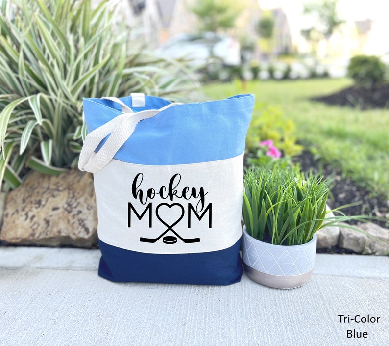 May include: A tri-color blue and white canvas tote bag with the text "hockey mom" and a hockey stick and puck graphic.