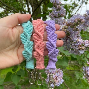 May include: Three colorful keychains made of braided string with silver key rings. The keychains are in shades of light blue, pink, and purple.