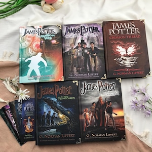May include: A collection of hardcover books titled "James Potter" with various sub-titles. The book covers feature illustrations of characters and scenes, with titles like "The Morrigan Web" and "Crimson Thread". The author's name, G. Norman Lippert, is also visible.