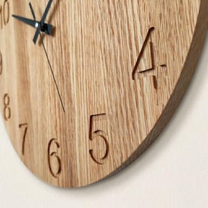 May include: Close-up of a wooden clock face with carved numerals. The clock hands are black, and the wood grain is visible. The numbers 4, 5, 6, 7, 8, and 10 are visible. The clock has a natural wood finish.