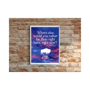 May include: A motivational quote by Marv Levy, "Where else would you rather be, than right here, right now?" printed on a framed poster with a white silhouette of a buffalo and the number 716. The poster has a blue and pink sunset background.