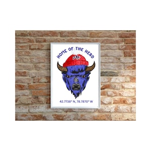 Può includere: Una stampa incorniciata bianca con un bufalo blu che indossa un cappello di lana rosso e bianco. La stampa dice "Home of the Herd" e "42.7738° N, 78.7870° W".