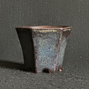May include: A dark grey hexagonal ceramic bonsai pot with a textured surface and a slightly raised rim. The pot has four small feet.