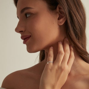 May include: A silver ring with a row of small clear stones and a dangling pear-shaped clear stone.