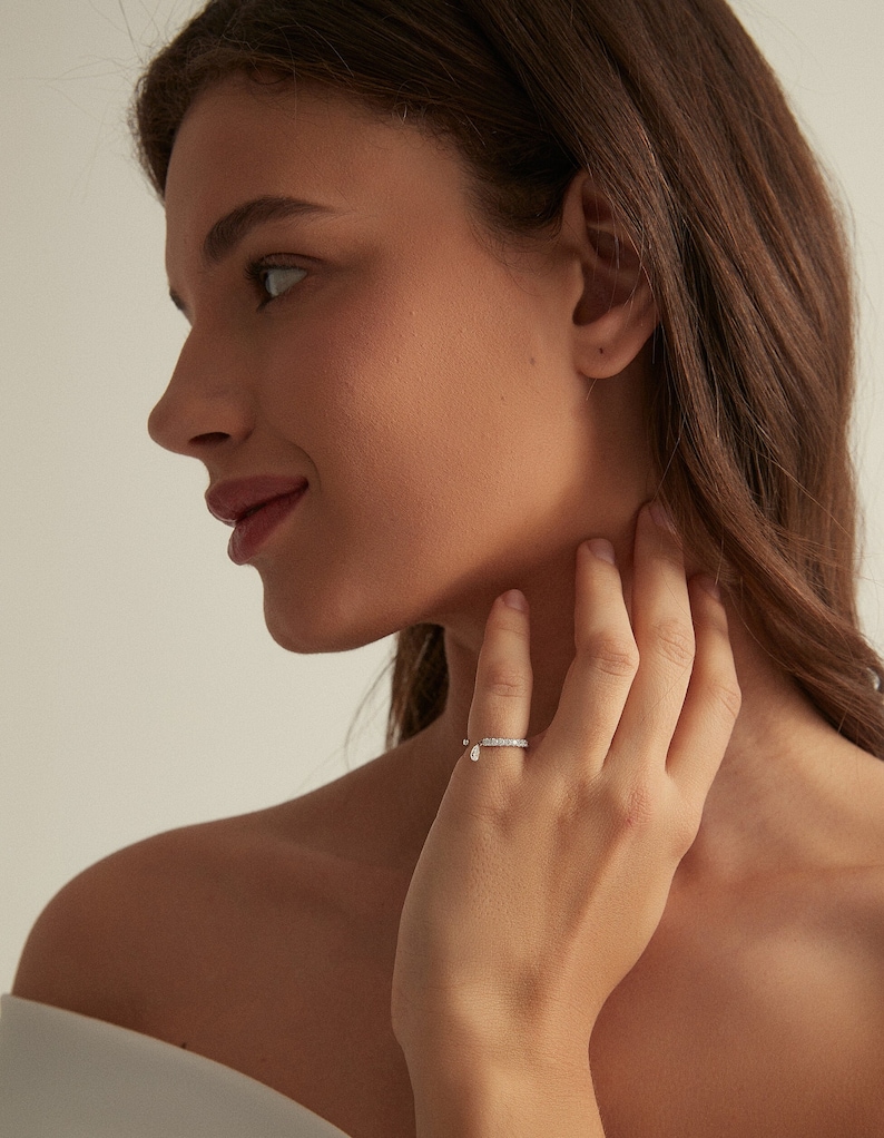 May include: A silver ring with a row of small clear stones and a dangling pear-shaped clear stone.