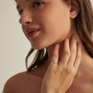 May include: A silver ring with a small diamond teardrop pendant. The ring is set with small diamonds and is worn on the ring finger of a person's hand.