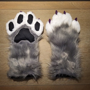 May include: A pair of gray wolf paw hand puppets with black paw pads and purple claws. The puppets are made of soft, fluffy fur.