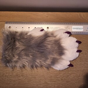 May include: A grey and white furry paw with purple claws. The paw is 35 cm long.