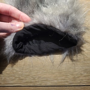 May include: Close-up of the inside of a grey faux fur pom pom. The pom pom is attached to a black fabric band.