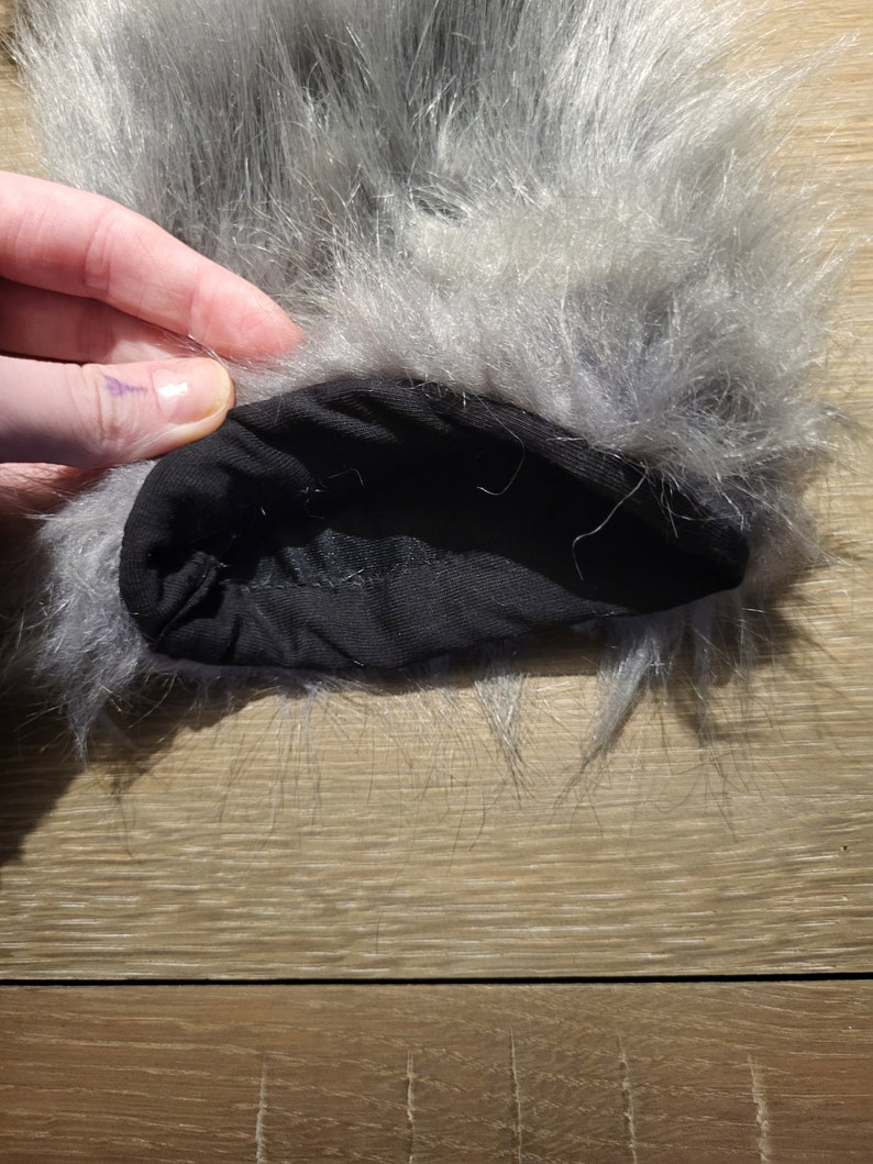 May include: Close-up of the inside of a grey faux fur pom pom. The pom pom is attached to a black fabric band.