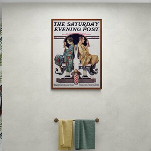 May include: A bathroom interior with two sinks and mirrors, each with a gold-toned faucet. The walls are covered in a tropical leaf wallpaper. A framed vintage magazine cover with the text "The Saturday Evening Post" hangs on the wall above the sinks.