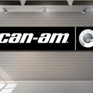 May include: A black rectangular banner with the white text "can-am" and a logo on a gray brick wall. The logo is a white gear inside a gray circle with the letters "BRP".