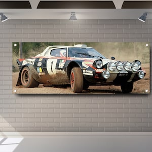 Puede incluir: Un coche de rally blanco, negro y naranja con la palabra "Lancia" en el lateral. El coche está conduciendo por un camino de tierra y tiene mucho polvo y tierra. El coche tiene un gran número "1" en el lateral.