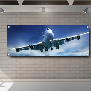 以下が含まれることがあります： 青い空と白い雲を背景に、白い飛行機が写っています。飛行機は着陸装置を下げてカメラに向かって飛んでいます。