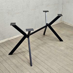 Könnte beinhalten: Schwarzes Metall-Tischgestell mit modernem, geometrischem Design. Das Gestell hat abgewinkelte Beine und rechteckige Montageplatten zur Befestigung einer Tischplatte. Die zentrale Stütze ist heller. Geeignet für verschiedene Tischgrößen.