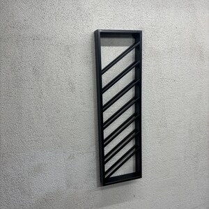 May include: A black metal wine rack mounted on a white wall. The rack has a diagonal design with multiple slots for storing wine bottles.