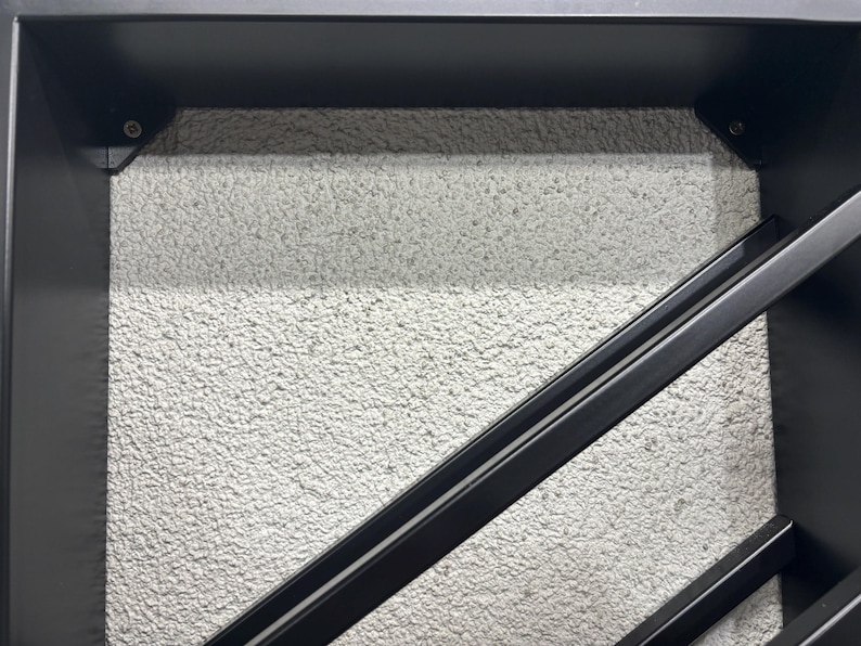 May include: Close-up of a black metal wine rack with a textured white background. The rack is made of two angled metal bars.