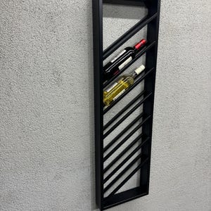 May include: Black metal wine rack with a diagonal design. The rack is mounted on a wall and holds two bottles of wine.