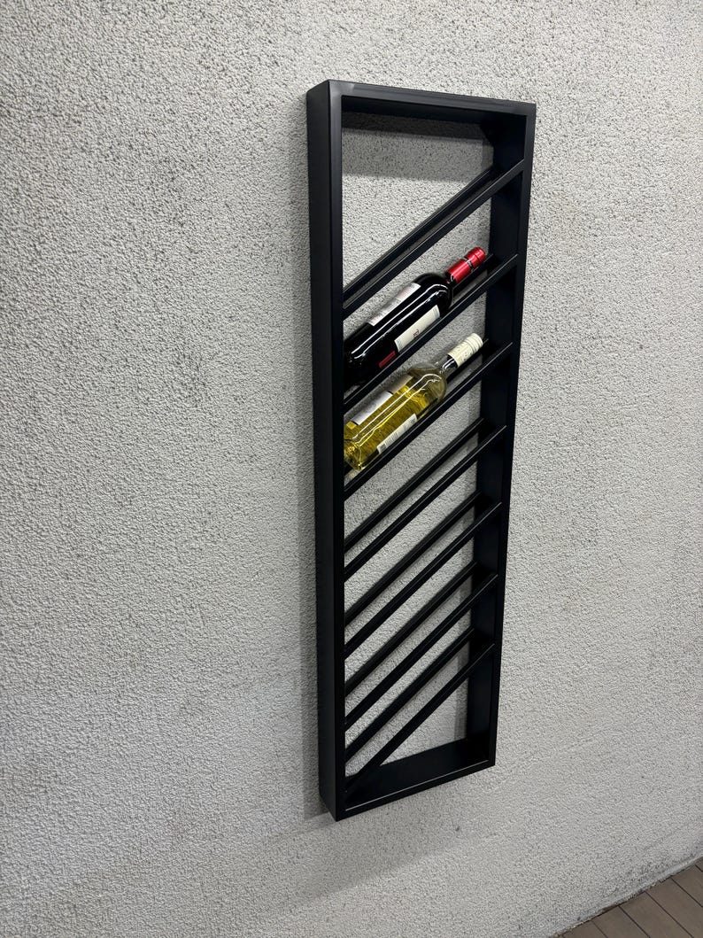 May include: Black metal wine rack with a diagonal design. The rack is mounted on a wall and holds two bottles of wine.