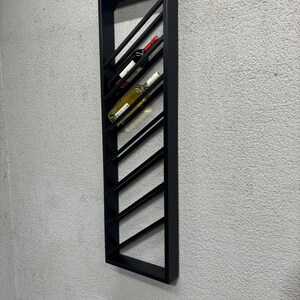 May include: Black metal wall-mounted wine rack with a diagonal design. The rack holds multiple bottles of wine.