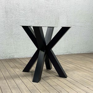 Può includere: Base per tavolo in metallo nero con un design a stella. La base ha quattro gambe che si estendono verso l'esterno e si incontrano in un punto centrale.