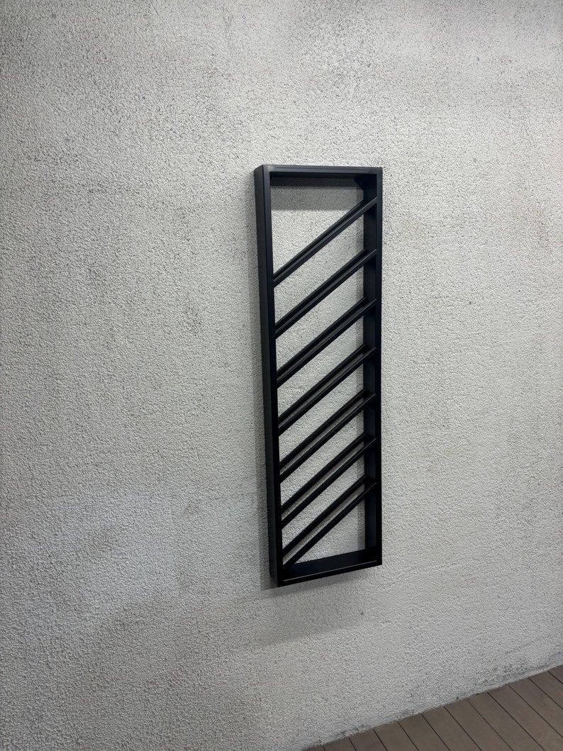 May include: A black metal wine rack mounted on a white wall. The rack has a diagonal design with multiple slots for storing wine bottles.