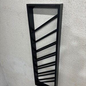 May include: Black metal wall mounted wine rack with a geometric design. The rack has 10 slots for storing wine bottles.