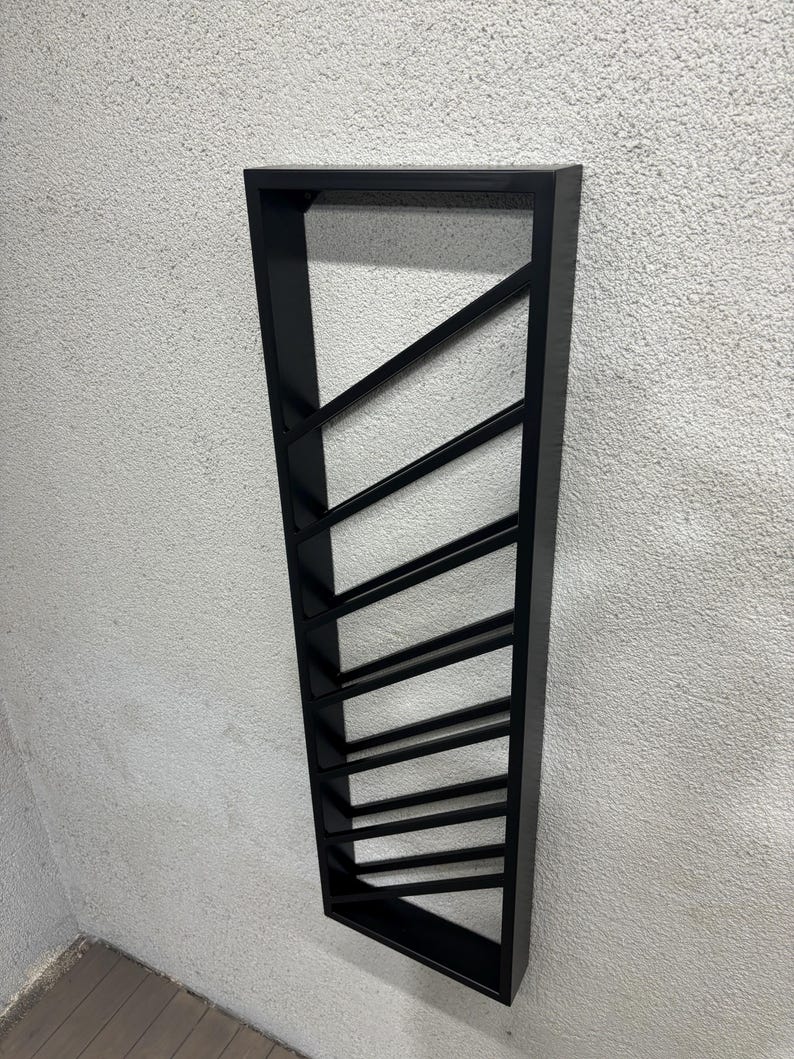 May include: Black metal wall mounted wine rack with a geometric design. The rack has 10 slots for storing wine bottles.