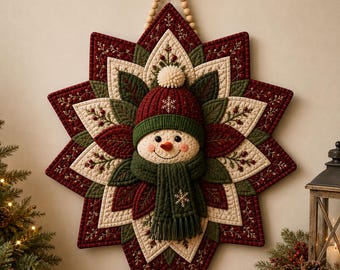 May include: A quilted wall hanging shaped like a large star with a central snowman face. The snowman wears a dark red knit hat with a white pom-pom and a dark green scarf. The star features layers of red, green, and cream fabric with embroidery.