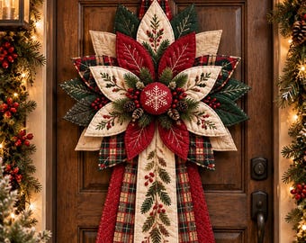 May include: A quilted Christmas door hanger featuring a star-shaped poinsettia design with red, cream, and plaid fabric petals. The centre has a red button with a white snowflake, surrounded by pine sprigs, berries, and long fabric tails.