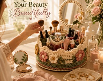 Puede incluir: Un organizador de maquillaje redondo de ganchillo en color crema con borde verde y flores decorativas rosas y blancas. El organizador incluye un espejo circular a juego en la parte superior y múltiples compartimentos llenos de productos de belleza.