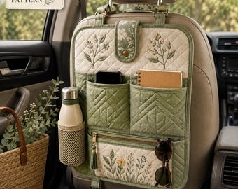 May include: A sage green quilted car seat organizer featuring floral embroidery, multiple storage pockets, a mesh water bottle holder, and a zippered compartment. The organizer includes a top flap with a snap closure and adjustable straps for attachment.