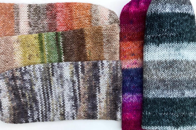 May include: Close-up of several knitted socks in various color combinations. The socks display a range of colors, including orange, brown, green, purple, and gray. The knitted texture is clearly visible, showcasing the craftsmanship of the socks.