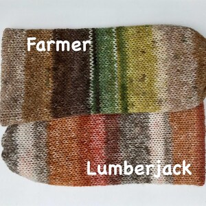 May include: Two knitted sock-like items, one labeled "Farmer" and the other "Lumberjack." The "Farmer" sock features brown, green, and tan stripes. The "Lumberjack" sock has red, orange, and brown stripes. Both are on a white background.