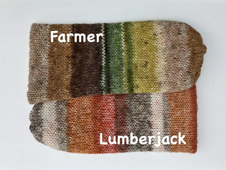 May include: Two knitted sock-like items, one labeled "Farmer" and the other "Lumberjack." The "Farmer" sock features brown, green, and tan stripes. The "Lumberjack" sock has red, orange, and brown stripes. Both are on a white background.