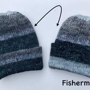 May include: Two knitted beanies in shades of gray, blue, and black, with a folded brim. The word "Fisherman" is written in black text below the beanies. The beanies are made of a soft, textured yarn.