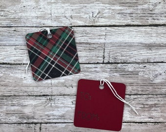 May include: Two square gift tags. One is burgundy with "TO: FROM:" in green stitching. The other is plaid with red, green, black, and white. Both have white string attached for hanging.