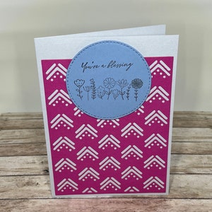 Könnte beinhalten: Eine weiße Karte mit einem rosafarbenen geometrischen Muster und einem blauen Kreis mit dem Text "You're a blessing" und einem kleinen Blumenmuster.
