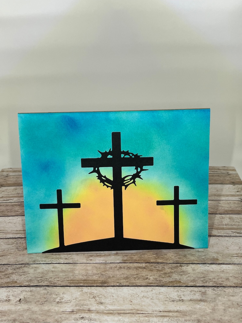 Pu&ograve; includere: Stampa su tela raffigurante tre croci nere stagliate su un cielo colorato. La croce centrale &egrave; adornata da una corona di spine. Lo sfondo sfuma dal blu al giallo, creando una scena serena e spirituale.